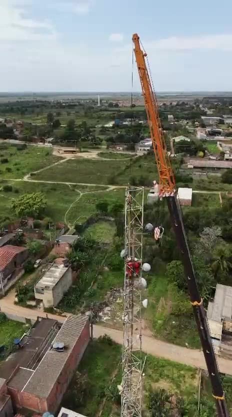 Vista aérea de içamento de torre com técnico em altura
